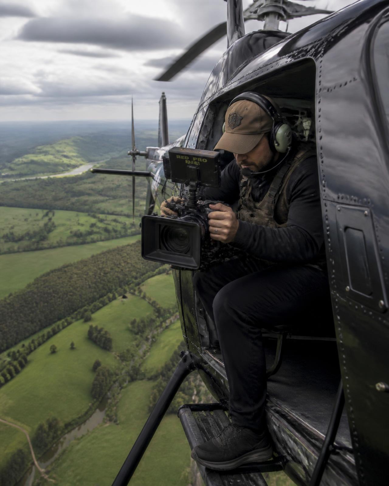 Camera operator filming from the open door of a helicopter in flight